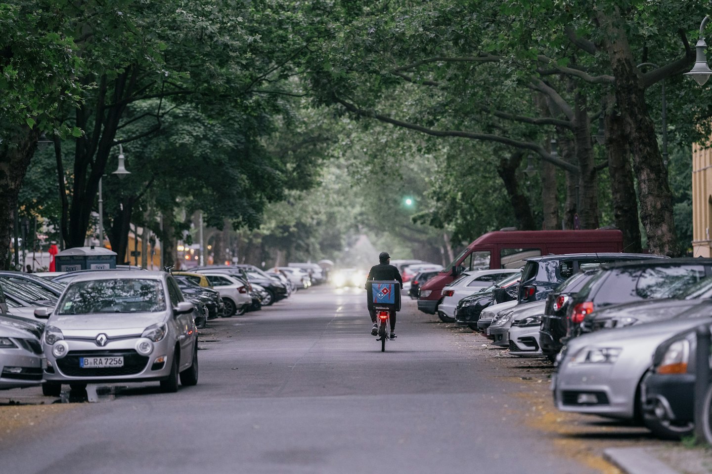 Un livreur à vélo avec une boîte bleue roule dans une rue de la ville.