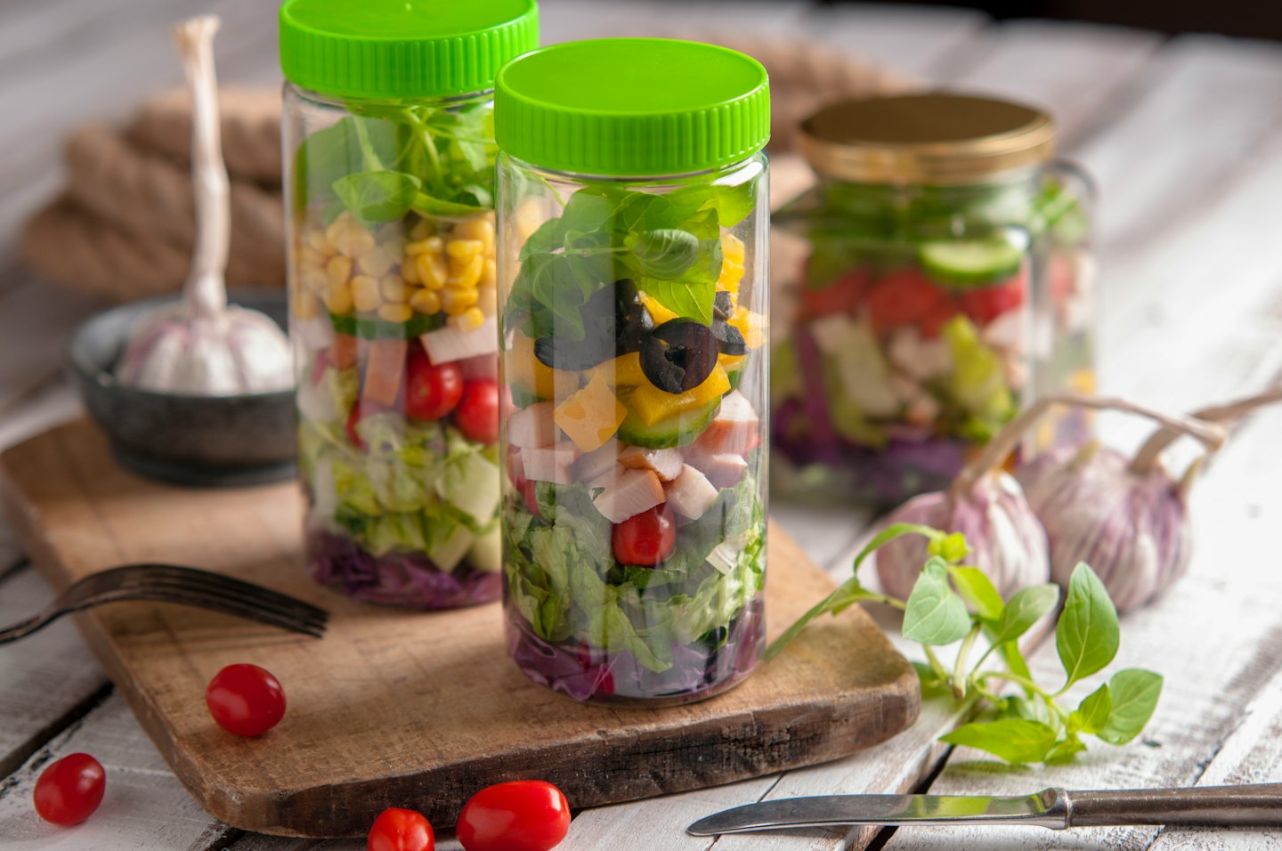 Trois bocaux en verre remplis de salades en couches sur une table en bois.