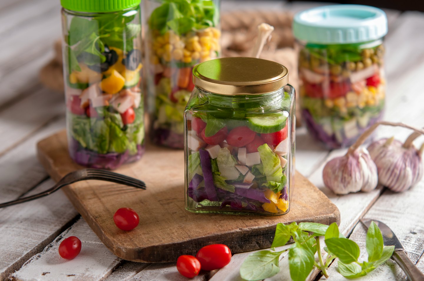Trois salades en couches dans des bocaux en verre sur une planche à découper en bois.