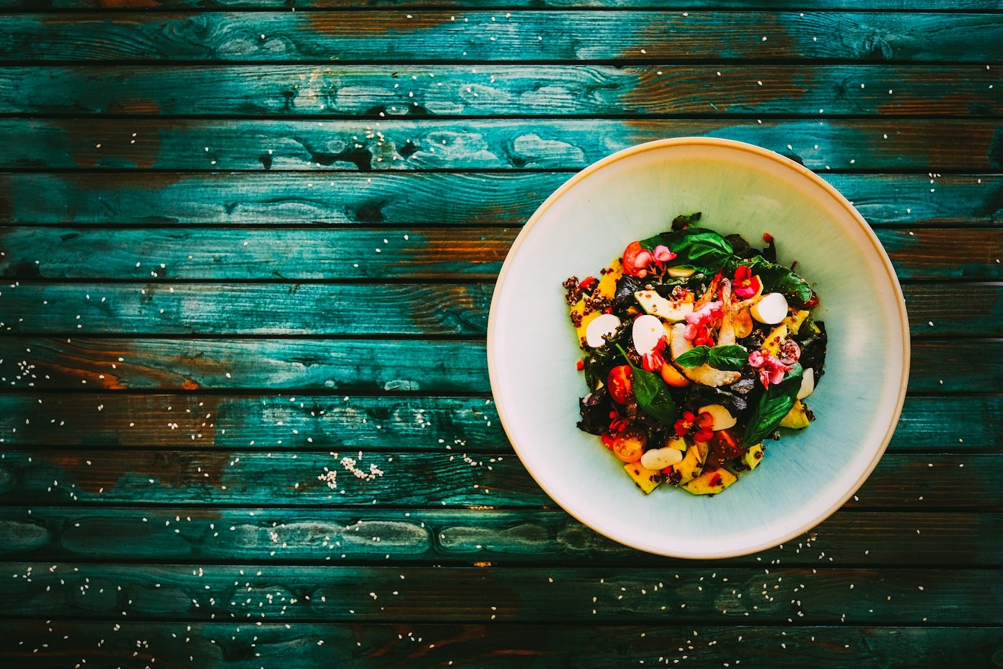 Salade colorée dans un bol bleu sur une table turquoise.