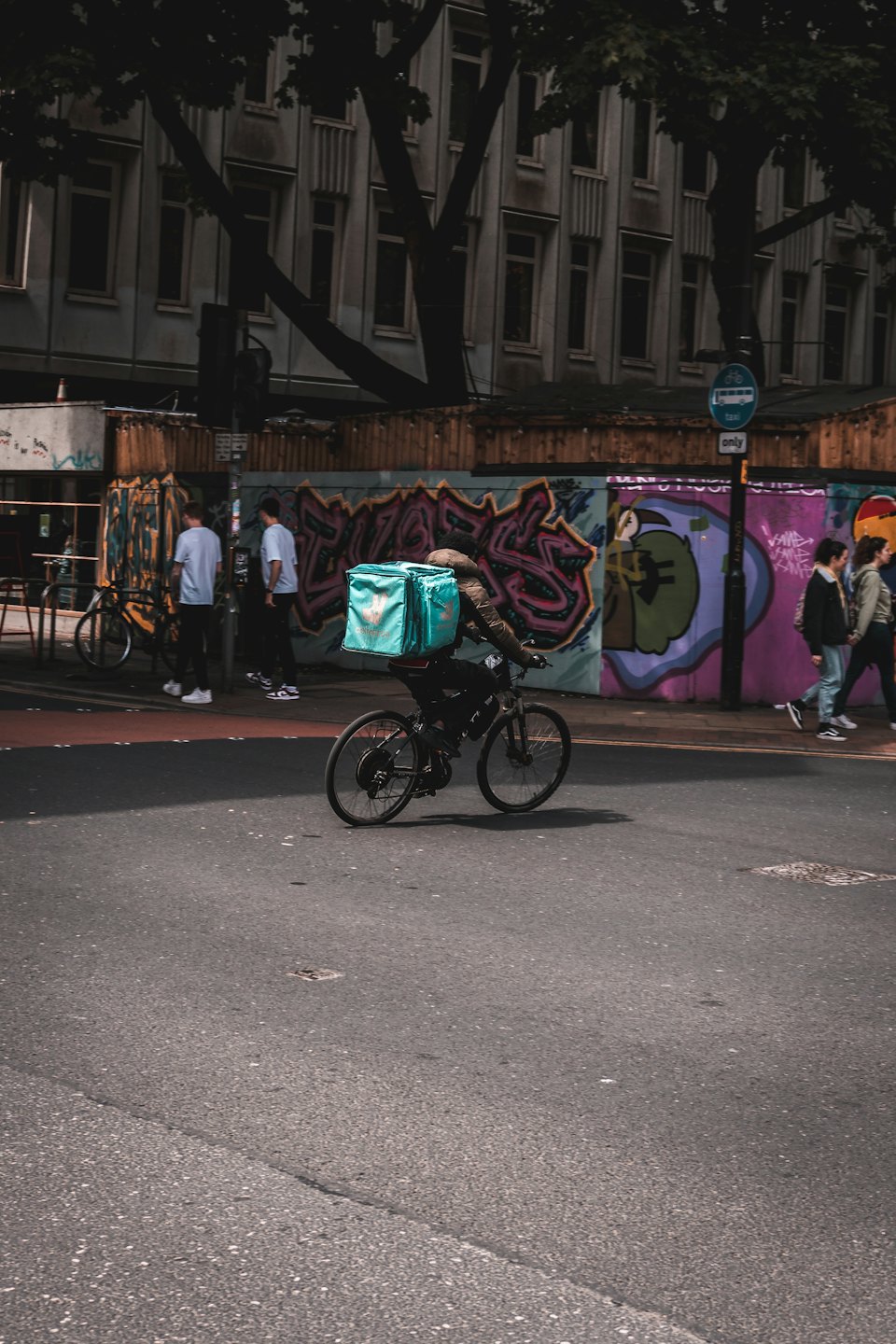 Un livreur à vélo descend une rue de la ville avec un sac turquoise.